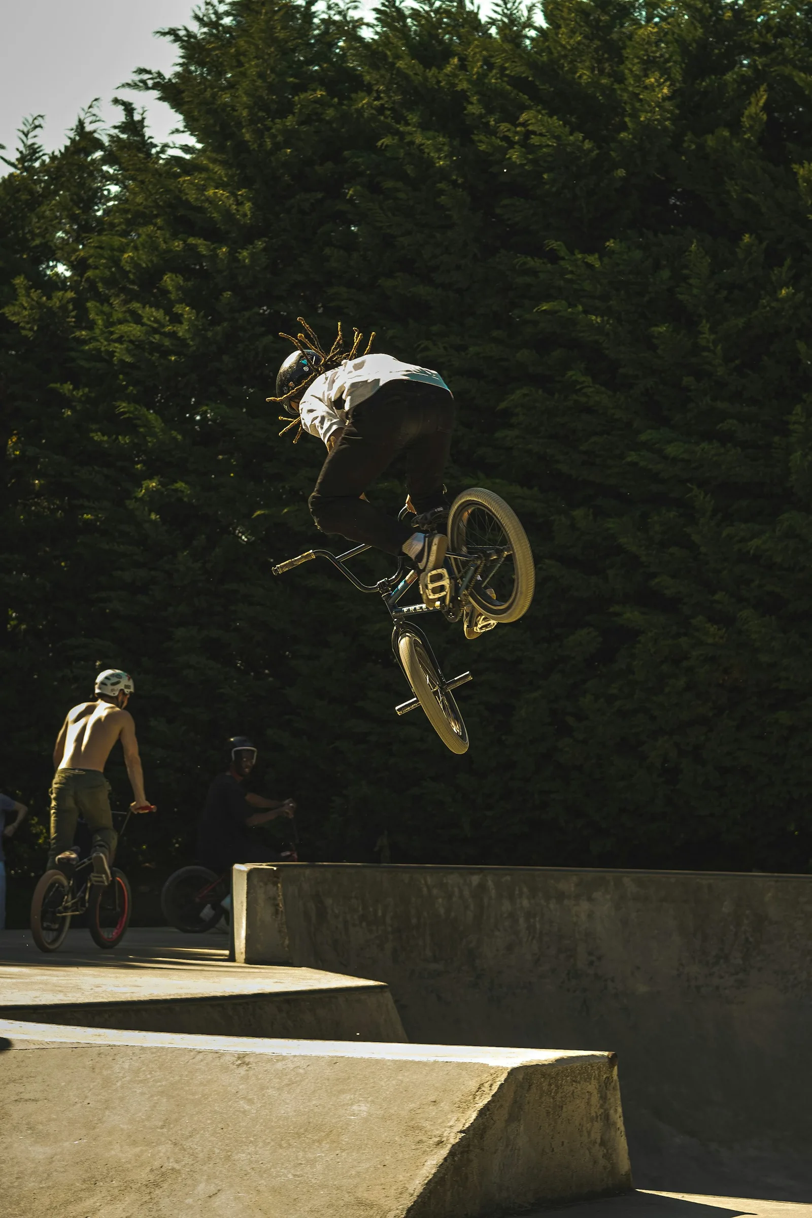 Un rider BMX en plein air au-dessus d’une rampe, sous le regard de son crew